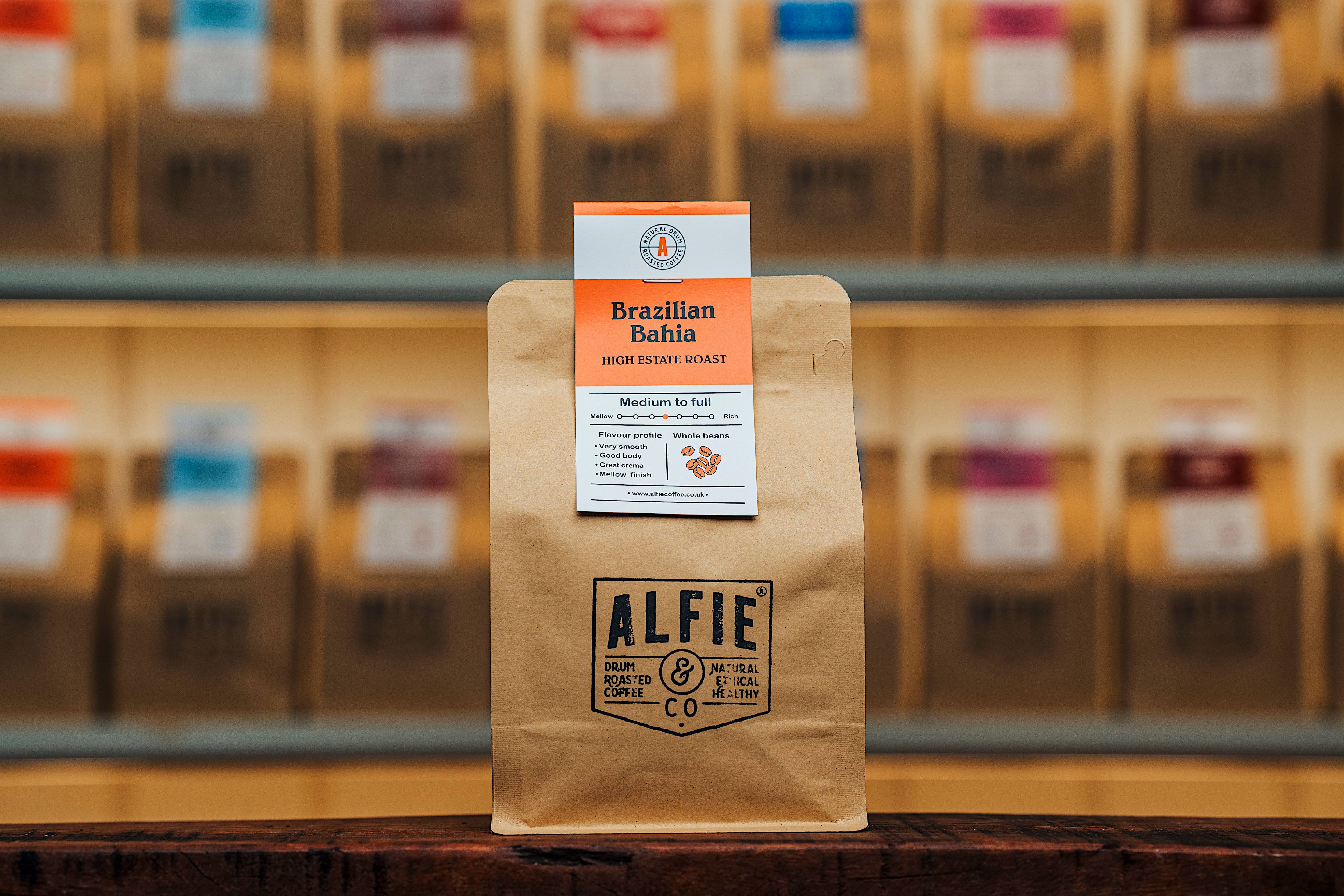 Alfie & Co Coffee Roasters – Brazilian Bahia whole-bean coffee in 250g kraft packaging, displayed on a wooden counter with softly blurred roastery shelves behind.
