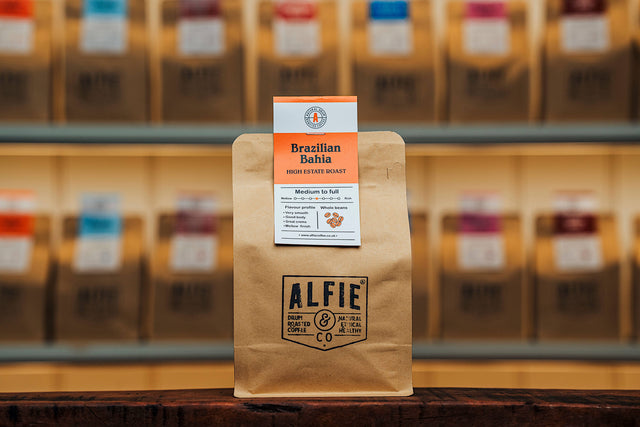 Alfie & Co Coffee Roasters – Brazilian Bahia whole-bean coffee in 250g kraft packaging, displayed on a wooden counter with softly blurred roastery shelves behind.

