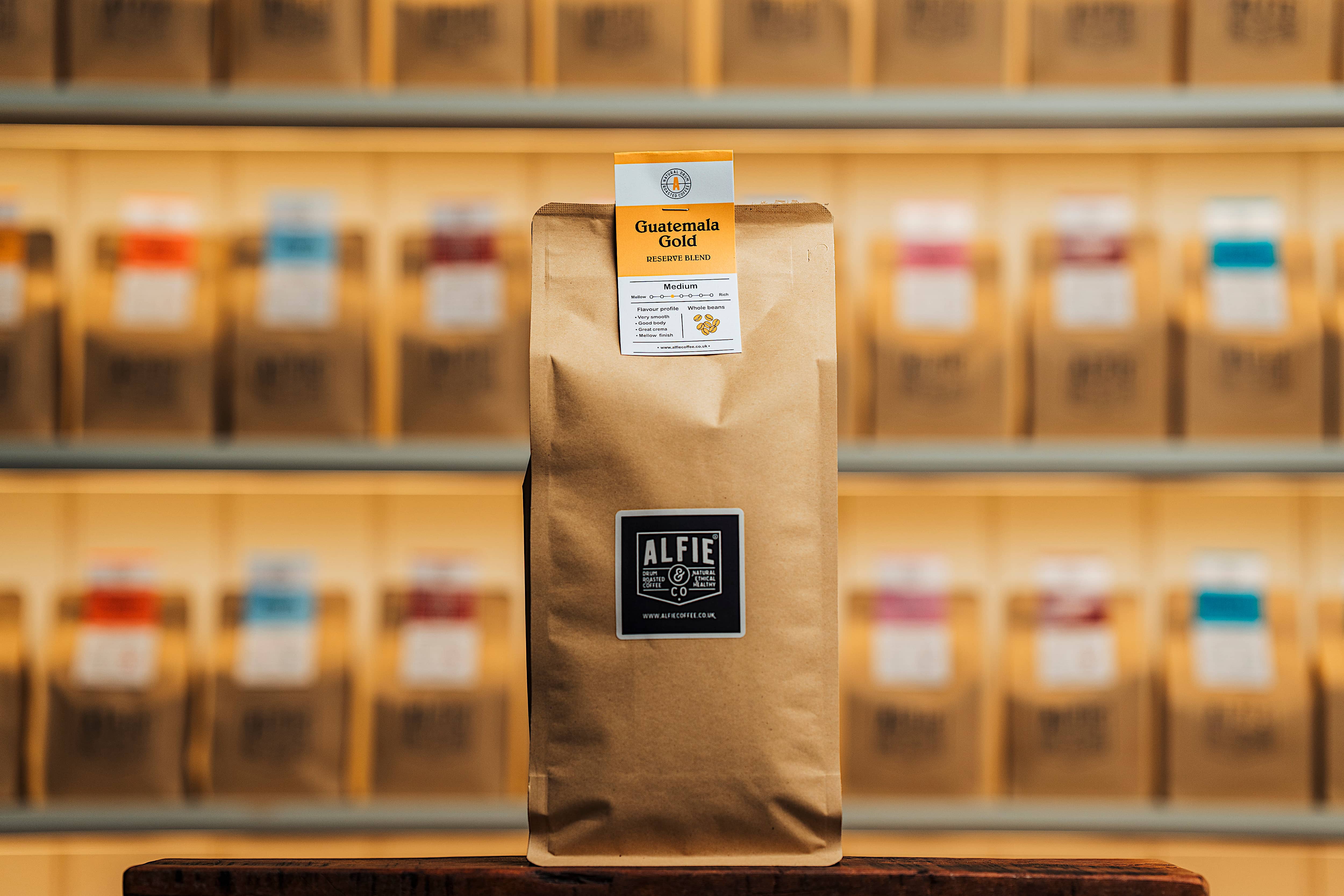 Alfie & Co Coffee Roasters – Guatemala Gold whole-bean coffee in 1kg kraft packaging, displayed on a wooden counter with softly blurred roastery shelves behind.