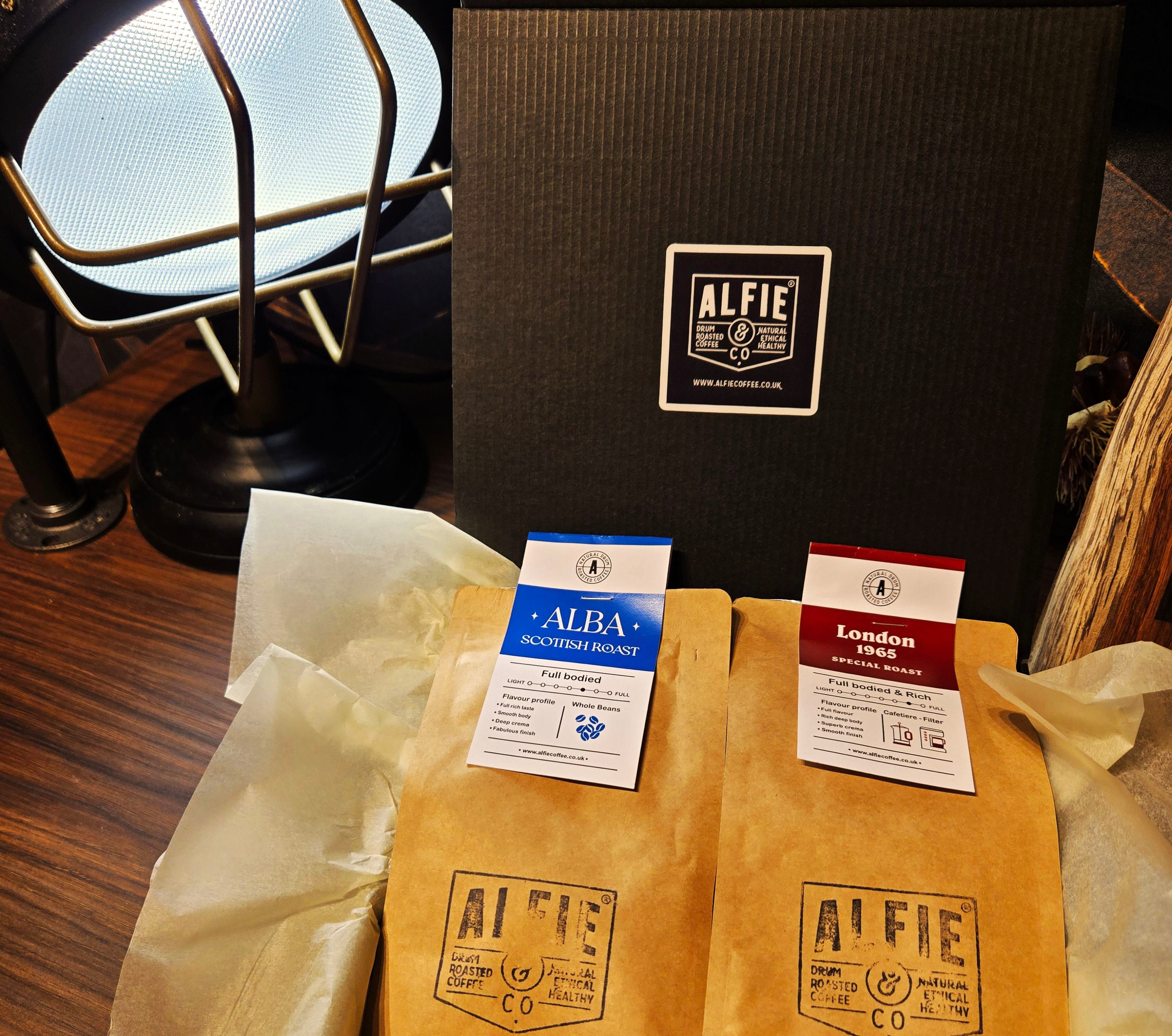 Alfie & Co. Alba and London 1965 coffee bags nestled in tissue paper within a sleek black gift box, featuring our logo.  This image showcases our premium coffee gift sets, perfect for any coffee lover.  Give the gift of hand-roasted, small-batch coffee from Killearn, Scotland, available for UK delivery at www.alfiecoffee.co.uk.  Highlights the thoughtful presentation and quality of our coffee gifts.