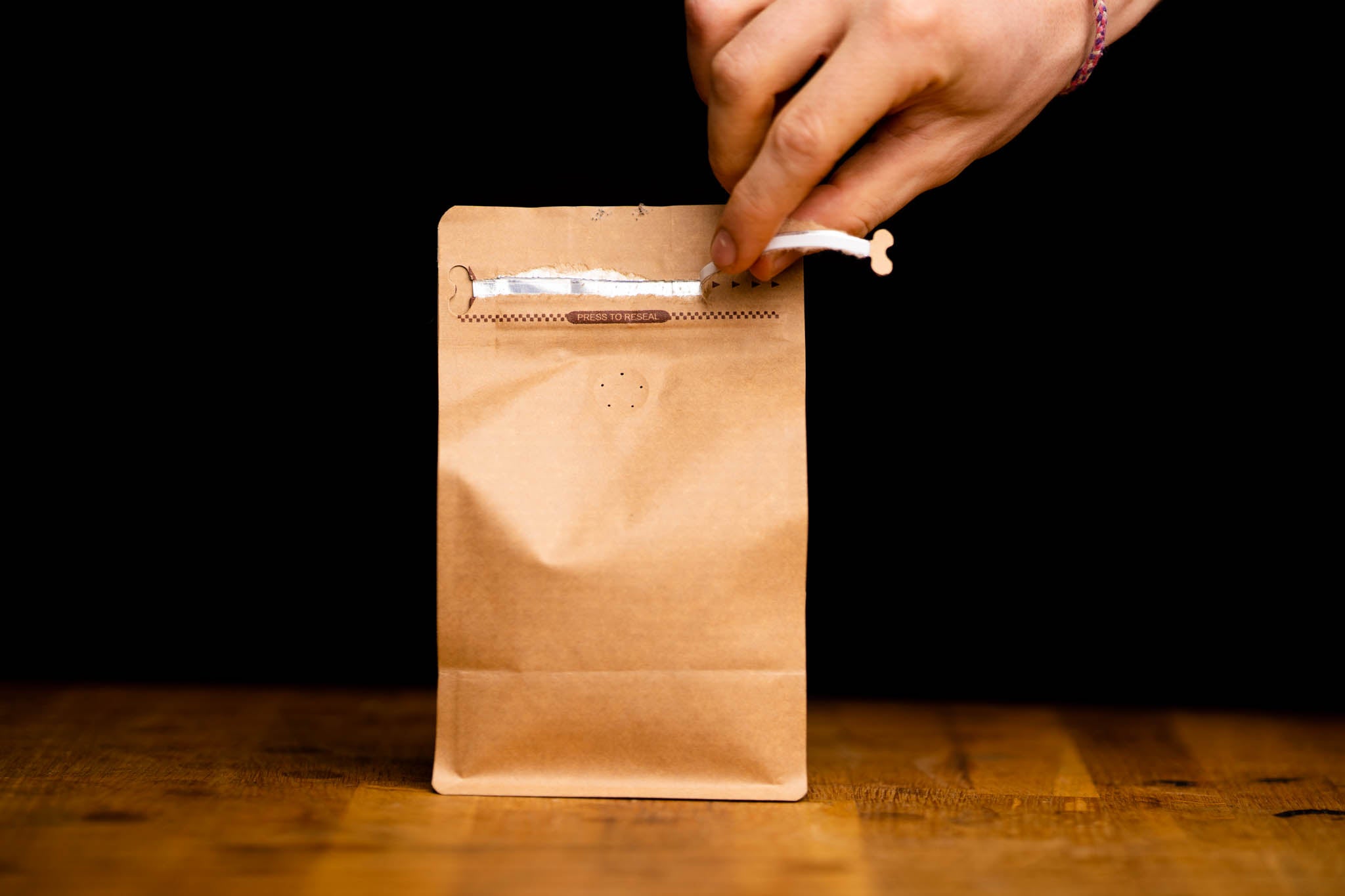 A hand resealing a kraft bag of Kindred Spirit coffee from Alfie & Co Coffee Roasters – fresh-roasted beans, naturally packaged and ethically sourced.